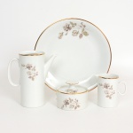 PORCELANA, conjunto para café com quatro (4) itens: 1 bule sem a tampa; 1 cremeira; 1 açucareiro e 1 prato para torta ou bolo, ornados com rosas em tons de cinza sobre fundo branco, arremates a ouro, manufatura RENNER (Porto Alegre, RS, fundada em 1942; em 1998 foi vendida para a Vista Alegre de Portugal; em 1999 mudou a razão social para Vista Alegre do Brasil), modelo MEDAILLON, medindo a maior peça 25,5 cm diâmetro, sinais de uso, vide foto.