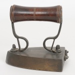 DIVERSOS, um (1) antigo ferro de passar roupa, confeccionado em bronze, cabo em madeira torneada, possui compartimento para colocar a pedra em brasa, pedra inclusa, medindo 11 x 12 x 7 cm, sinais de uso, vide foto.