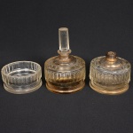 FLACONS DE PARFUM, três (3) antigos recipientes confeccionados em cristal, incolores e translúcidos, lapidação canelada na vertical, remanescentes de conjunto para toucador, um deles com bicado na borda, mossa no fundo, tampa com bicados na parte interna e desgastes ou perdas na parte superior, outro com monture em metal faltando bomba aspersora; 1 pote sem a tampa com sinais de raspado, todos com arremates a ouro já com sinais de desgastes, medindo aproximadamente 10 cm diâmetro, sinais de uso, vide foto.