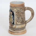 PORCELANA, uma (1) caneca com ornamentação relevada na própria modelagem, representando cena de taberna e parras, policromada, fundo azul cobalto, manufatura CERAMARTE (Rio Negrinho, SC, fundada em 1956 pelo alemão Klaus Schumacher, ainda em atividade), medindo 13,5 cm altura, vide foto.