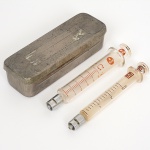 DIVERSOS, uma (1) antiga caixa em metal com duas seringas em vidro, medindo 11 cm comprimento, sinais de uso e mossa, vide foto.