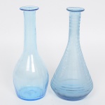 Duas(02) garrafas em vidro soprado, tonalidade azul. Necessita repor as tampas. Meds.: Alt. 21,5 x Diam. 8,5 cm; Alt. 21,5 x Diam. 10 cm.