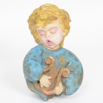 Escultura de parede executada em estuque policromado, representando figura angelical tocando lira, apresenta cabelos modelados e pintados em tom amarelo/dourado, rosto com olhos fechados e boca aberta, sugerindo canto. Apresenta sinais de desgaste e pintura com pequenas marcas e descascados, vide foto. Parte traseira com gancho para fixação em parede. Med.: Alt. 19,5 x Comp. 12 x Larg. 7 cm.