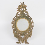 Antiga moldura para espelho executada em bronze, centro circular contornado por perolados em relevo, encimada por flores, decoração com padrão floral e vegetalista obtidas através das técnicas do cinzelado e repuxado, necessita colocação do vidro. Partr traseira dotada de haste para apoio. Med.: Alt. 37,5 x DUIaml. 8 cm