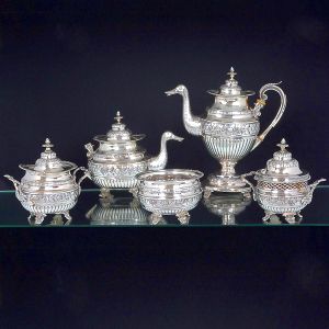 Belíssimo <b>serviço para chá e café </b>em prata portuguesa repuxada e cinzelada, decorada em estilo neoclássico com frisos gomados, flores e folhagens. Pegas das tampas modeladas em pinhas e pés em volutas. Alças dos bules em madeira e bicos modelados em cabeças de pato. Constando de bule para café, bule para chá, açucareiro, biscoiteira e "bowl". Contraste da cidade do Porto de LUIS ANTONIO RODRIGUES DE ARAÚJO (1843 a 1853) e marca de prateiro. Falta alça do bule de chá. Peso 4400 gramas. Alt. do bule de café 34 cm