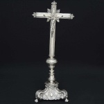 Belíssimo <b>crucifixo</b>  em prata espanhola do séc. XVIII. Cruz filetada no sentido vertical com ponteiras estilizadas e pequenos raionados na parte posterior. A imagem do crucificado apoia-se sob florão com botão de flor ao centro. Haste movimentada e base trípode terminada em pés de garras sobre esferas. Belíssimos trabalhos lavrados em rocalhas e volutas em composições barrocas. Contraste da cidade de Córdoba de 1732.