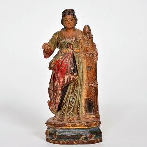 Imagem de <B>Santa Bárbara </B>em madeira entalhada e policromada, apoiada sobre base octogonal. A Santa apresenta-se de pé, vestindo túnica em verde, e mangas longas, cingida à cintura por cinto dourado. Sobre ela recai manto vermelho, drapeado em amplos pregueados diagonais, com vestígios de douração a ouro. À lateral direita ergue-se torre ameada, atributo iconográfico que alude ao cárcere do martírio. Alt. 17 cm