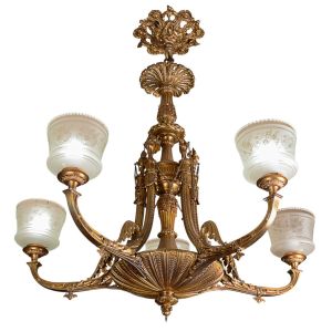 <b>Lustre </b>clássico em metal dourado, ricamente trabalhado com elementos fitomórficos e volutas, apresentando cinco braços curvos delicadamente ornados. Corpo central com fuste canelado e cúpula inferior em gomos, arrematada por pingente torneado. Ligações decoradas com correntes metálicas e pináculos. Cúpulas em vidro leitoso com bordas rendilhadas e finos adornos florais gravados. Alt. 110 cm