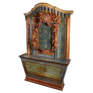 Magnífico e grande <b>altar de capela </b>ricamente policromado em tonalidades de azul e vermelho. Apresenta parte superior em arcada decorada com bilros. Ao centro exuberante baldaquim encimado por belo panejamento, fundo florido e ladeado por entalhes com anjos, elementos concheados e volutas. Mesa de celebração decorada com florão ao centro. Séc. XVIII. Med. 285 x 190 x 46 cm