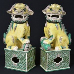 <b>Par de "cães de fó" </b>em porcelana chinesa esmaltada e policromada nas cores amarelo, verde e lilás, com detalhes em alto-relevo. Tradicionais leões guardiões chineses, modelados em postura vigilante, cada um apoiando a pata sobre esfera simbólica e base retangular ricamente decorada com motivos florais geométricos entrelaçados. Um apresenta restauro na orelha. Alt. 43 cm