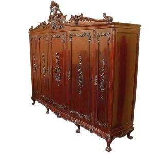 <b>Guarda-roupa </b>em jacarandá, de grande porte e rica talha em estilo Luís XV. Frente composta por cinco portas almofadadas com entalhes em volutas e motivos fitomórficos, arrematadas por ferragens douradas. Coroamento superior com frontão recortado em desenho de concha e arabescos. Base recortada apoiada sobre pés "cabriolet" com garras e folhagens. Med. 236 x 263 x 60 cm