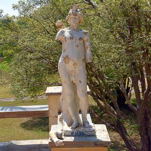 <b>Escultura </b>em faiança representando "Brazil". Figura feminina em posição ereta sobre base retangular, portando cocar indígena e manto esculpido em relevo, apoiada sobre tronco de árvore. Marcada na base com a inscrição " F. Devezas / Valente/ Brazil". Um dos braços quebrado e perdas significativas no verniz e na modelagem, com craquelê evidente em toda a superfície.