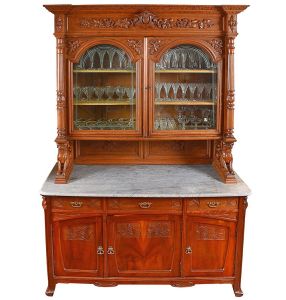 <b>Guarda louças </b>em madeira entalhada com tampo em mármore. Parte superior com duas portas envidraçadas em arco, ladeadas por colunas torsas e ornada por frisos florais em relevo. Base apresenta gavetas e portas com entalhes vegetalistas, apoiadas sobre tampo em mármore cinza. Laterais decoradas com figuras  de cachorros esculpidas. Med. 255 x 166 x 65 cm