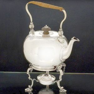 Rara "<b>tea kettle</b>" de forma globular em prata inglesa do período George II. Timbre armorial na face anterior e borda gravada com composições estilizadas. Triplas pernas em curvas e contracurvas com pés concheados. Pega da tampa em madeira e alça móvel em vime. Contraste da cidade de Londres de 1736. Peso 1.500 gramas. Alt. com a alça em pé 31,5 cm