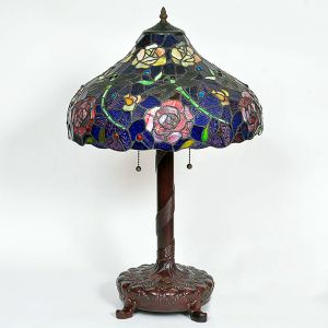<b>Luminária </b>estilo Tiffany, com cúpula em composição de vidros policromados no padrão "vitraux", formando delicados motivos florais em tons de azul, lilás, rosa e verde. Estrutura em metal patinado com fuste em formato de coluna torcida e base decorada com relevos vegetalistas. Acionamento por duas correntes com esferas metálicas. Alt. 70 cm
