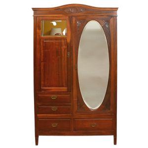 <b>Guarda-roupa </b>em madeira nobre, com frente assimétrica composta por porta com espelho oval bisotado e outra lisa superior com pequeno espelho retangular. Parte inferior com gavetas de diferentes formatos, dotadas de puxadores metálicos. Aplicações entalhadas em motivo floral nos cantos do espelho e na pala superior. Med. 202 x 118 x 48 cm