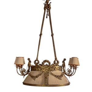 <b>Lustre </b>em metal dourado ricamente trabalhado, com fuste sustentado por quatro hastes em forma de cordões entrelaçados, decorado com figuras femininas, grinaldas florais e elementos neoclássicos. Corpo central com cúpula revestida em tecido plissado creme e seis braços laterais com "bobèches" e cúpulas individuais. Med. 123 x 86 cm