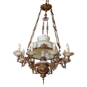 <b>Lustre </b>em metal dourado ricamente trabalhado, com ornamentos fitomorfos e reservas em relevo figurando cenas arquitetônicas. Estrutura com oito braços para vela eletrificada, com "bobèches" em vidro leitoso moldado em volutas. Corpo central com cúpula também em vidro leitoso. Suspenso por correntes duplas decoradas. Alt. 120 cm