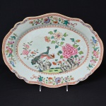 <b>Travessa </b>de forma oval e bordas recortadas, em porcelana Companhia das Índias, Família Rosa, pertencente ao Serviço Real de D. João VI, conhecido como Serviço dos Pavões. Centro apresentando dois pavões, sobre um rochedo, cercados de peônias. Borda em flores e arabescos. Séc. XVIII. Apresenta restauro. Compr. 35 cm