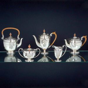 <b>Serviço de chá e café </b>em prata inglesa, apresentando peças lisas com bojos facetados e pegas em madeira torneada. Constando de "tea kettle" (falta a base), bule de café, bule de chá, leiteira e açucareiro. Contrastes da cidade de Sheffield de 1920 e marca de prateiro. Alt. do bule de café 22 cm. Peso: 2590 grs