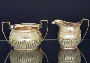<b>Conjunto de açucareiro e leiteira </b>em prata escocesa do período George III. Decoração neoclássica com gomos à meia altura e monograma ao centro. Contraste da cidade de Edimburgo de 1800 e marca do prateiro W & P CUNNINGHAM. Alguns amassados do tempo. Alt. do açucareiro 10 cm; Compr. 16,5 cm. Peso 387 gramas.