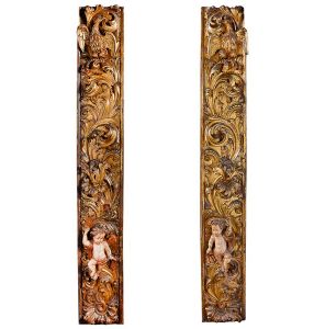 Extraordinário <b>par de talhas </b>em madeira patinada com douração de época e decoradas em ricas composições de motivos vegetais. Ao topo a representação de um pelicano simbolizando Jesus Cristo, ícone do sacrifício supremo. À parte baixa destacam-se figuras de anjos com pátina clara, carmim e ouro. Alt. 240 cm