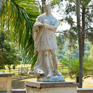 <b>Escultura </b>em faiança vitrificada, representando figura alegórica de "América", em pé, portando cocar e saia estilizada em formato de folhas, com peleja enrolada ao redor do corpo, apoiada sobre golfinho. Inscrições "Fª S?? Antônio  Porto". Apresenta desgastes e pequenas perdas no esmalte.