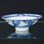 <b>Covilhete </b>circular sobre base elevada, em porcelana azul e branco, decorado internamente com reserva central com paisagem estilizada e borda com motivos florais contínuos. Parte externa com representação de figuras em paisagem. Apresenta bicados e trinca visível na aba. Diâm. 14 cm