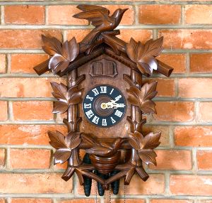 <b>Relógio de parede </b>em madeira entalhada, representando casa alpina adornada por folhas e pássaros, com mostrador circular em fundo negro, algarismos romanos aplicados e ponteiros trabalhados em metal dourado. Mecanismo de corda acionado por pesos em formato de pinha. Alt. 45 cm