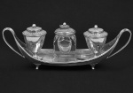 <b>Tinteiro </b>em prata inglesa do período George IV. Base ovalada com alças laterais filetadas. Recipiente em cristal (bicado na base e tampa com amassado) centralizado por dois outros em forma de urnas. Contrastes da cidade de Londres de 1828 e marca de prateiro. Compr. 26,5 cm
