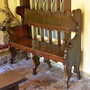 <b>Banco </b>em madeira entalhada, ao gosto colonial luso-brasileiro, apresentando encosto recortado em volutas com entalhes em baixo-relevo e braços laterais fechados, em rocalhas. Assento reto apoiado sobre base com saia e pés recortados. Med. 112 x 145 x 42 cm