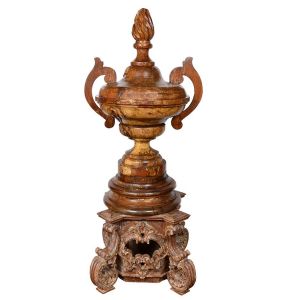 Belo <b>capitel </b>em forma de urna com duplas alças em madeira. Apresenta parte superior modelada em labaredas.  A peça apoia-se sobre base diversa de época anterior em madeira entalhada, motivos barrocos e vestígios de pátina. Séc. XVIII / XIX. Alt. 182 cm