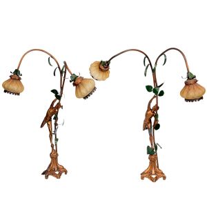 <b>Par de luminárias </b>de mesa em metal dourado patinado, com estrutura sinuosa em forma de trepadeira com aplicações de folhas esmaltadas e figura feminina escalando o fuste. Cada peça com duas cúpulas em vidro opalino modelado em forma de flor. Alt. 71 cm