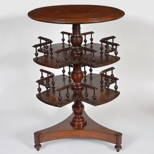 <b>Mesinha lateral giratória </b>em madeira entalhada, com tampo circular e três prateleiras octogonais sobre fuste central torneado. Estrutura com pequenos balaústres formando divisórias laterais. Base triangular com pés boleados. Med. 81 x 49 cm