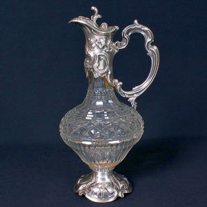 "<b>Claret jug</b>" em cristal francês, provavelmente Baccarat, apresentando montagem em prata portuguesa decorada com volutas e botões de flores em relevo. Contraste "Águia" da cidade do Porto, marca de prateiro e da joalheria Topázio. Alt. 31 cm