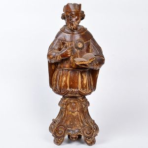 <b>Busto</b> em madeira entalhada, de concepção invulgar, representando apóstolo com relicário. A imagem traz um livro à mão sugerindo tratar-se de santo doutor. Resquício de douração. Base trípode com decoração barroca. Séc. XVIII. Alt. 55 cm