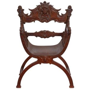 <b>Cadeira savonarola </b>em madeira nobre profusamente entalhada. Estrutura de linhas curvas, com braços e traves decorados por entalhes vegetalistas em relevo. Cartela central e apoios inferiores decorados com máscaras. Med. 100 x 71 cm