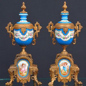 <b>Par de ânforas </b>em porcelana francesa policromada, com guirlandas de flores na parte superior e reservas frontais representando "putti", na inferior. Guarnições e bases em bronze dourado ornadas com elementos fitomorfos. Alt. 36 cm
