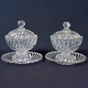 <b>Par de compoteiras com seus pratos </b>em cristal francês "Baccarat", moldados com gomos torcidos. Bojos semiesféricos com bases cônicas. Tampas abobadadas e pires no estilo. Marcas da "Cristallerie" em todas as peças. Alt. 19 cm