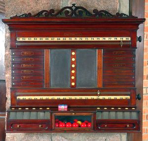 <b>Marcador de jogo de sinuca</b>  em madeira nobre, ricamente trabalhado, com plaquetas numeradas, lousas centrais, gavetas e compartimentos para armazenamento das bolas. Estrutura encimada por lambrequim vazado. Med. 93 x 108 cm
