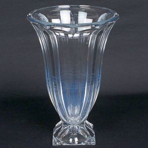 <b>Vaso </b>em cristal lapidado, de corpo cilíndrico levemente afunilado, decorado por gomos verticais. Borda superior espessa e boleada, apoiado sobre base quadrada facetada. Apresenta lascados nos cantos da base. Alt. 36 cm