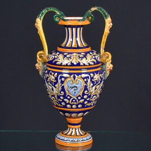 <b>Vaso </b>em cerâmica policromada com decoração em estilo renascentista, bojo ricamente ornado com volutas, escudos e máscaras laterais. Alças modeladas com figuras mitológicas. Apresenta quebras na base e nas alças. Alt. 39 cm