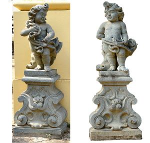 <b>Par de esculturas de anjos </b>esculpidos em pedra sabão, apoiados sobre base integrada com volutas em relevo. Esculturas de fatura recente, inspiradas em modelos barrocos, apresentando traços infantis e panejamento marcado.