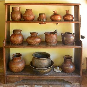 <b>Móvel poteiro </b>rústico em madeira, composto por três prateleiras, acompanhado de conjunto com 12 potes e 4 conchas em cerâmica de queima baixa. Peças com rica pátina e variações tonais. Med. do móvel 180 x 158 x 46 cm