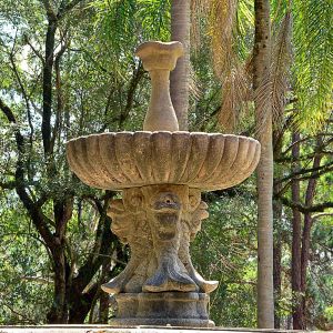 <b>Chafariz </b>em pedra lavrada, composto por ampla bacia em gomos apoiada sobre base com quatro figuras de carpas estilizadas em relevo. No centro, coluna torneada encimada por elemento floral em forma de taça.