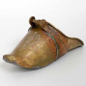 <b>Sapata </b>em bronze fundido, de formato alongado e ligeiramente abaulado, com extremidade frontal arredondada e gravações decorativas finamente executadas em arabescos e entrelaces geométricos. Compr. 21 cm
