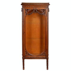 <b>Móvel vitrine </b>em madeira nobre ricamente entalhada, de estilo clássico. Estrutura com laterais decoradas por entalhes de folhagens e flores, ladeadas por frisos geométricos. Med. 175 x 65 x 37 cm