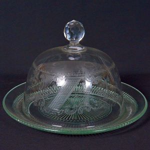 <b>Queijeira </b>em cristal lapidado. Prato de borda trabalhada sustentando cúpula transparente adornada por delicados arabescos gravados. Puxador facetado ao topo. Alt. 19 cm ; Diâm. do prato 28 cm