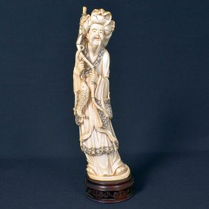 <b>Escultura japonesa </b>em marfim, representando ancião portando cajado e peixe, símbolos de longevidade e prosperidade. A peça repousa sobre base de madeira entalhada. Apresenta selo. Alt. 34 cm