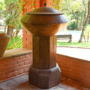 <b>Pilão </b>antigo em madeira maciça, de grandes proporções, composto por base octogonal encorpada e recipiente superior de formato abaulado, com tampa igualmente em madeira torneada. Alt. 120 cm